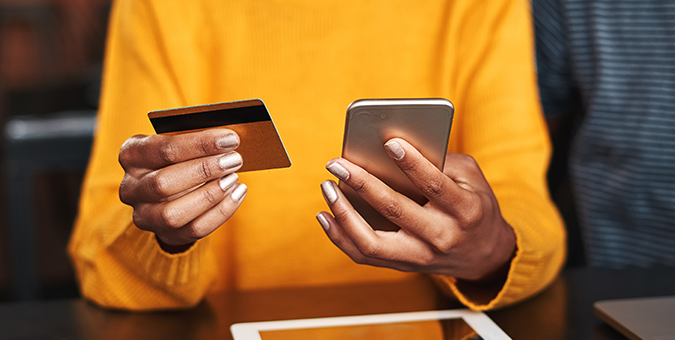 person in an orange sweater holding a credit/debit card and their mobile phone