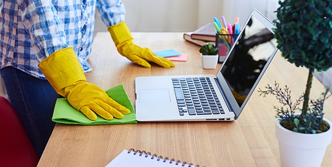 a person with yellow cleaning gloves cleaning a work desk